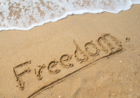 Photo of the word Freedom spelled into the sand on the beach.