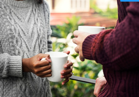 Photo of a woman and man talking outside wearing sweaters and drinking coffee.
